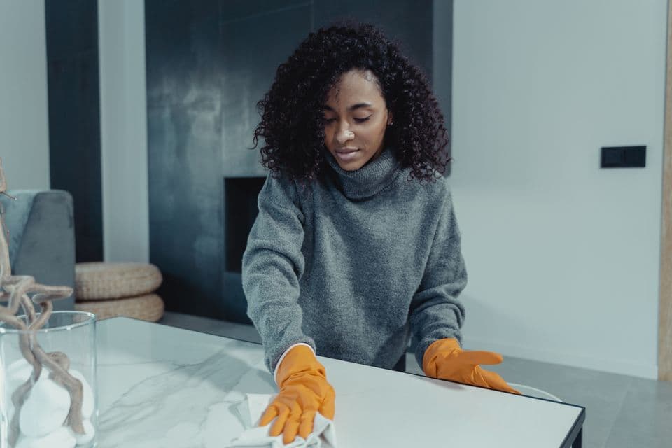 A woman wiping a table with cleaning gloves