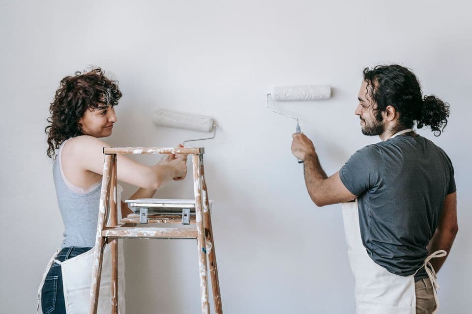 Two people painting a wall with rollers