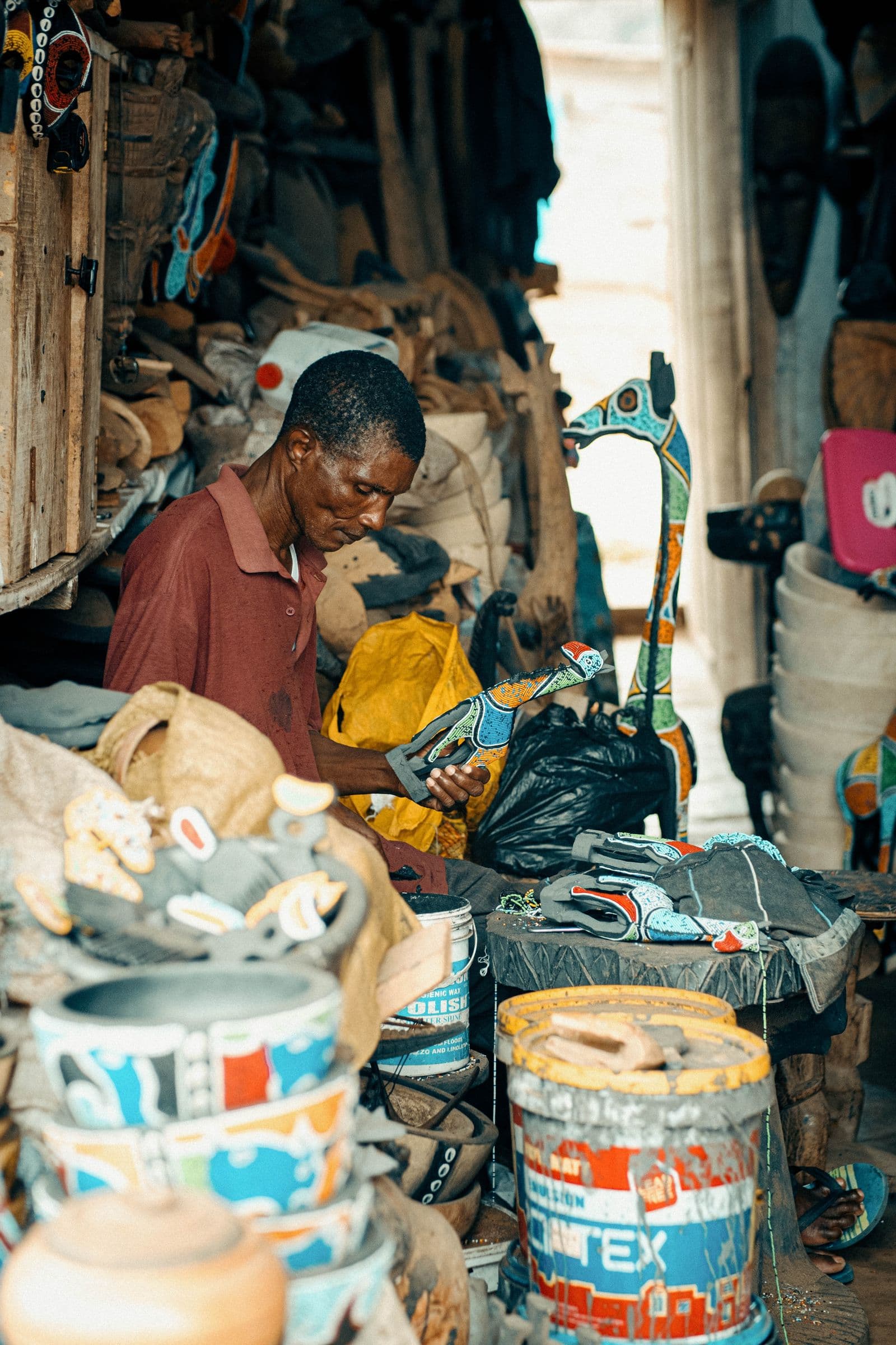 A craftsman carving colourful wooden sculptures at a market in Kumasi