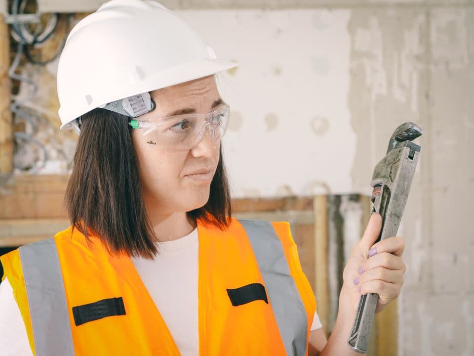 A worker in a hard hat holding a pipe wrench